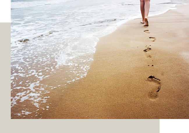 Person leaving footsteps in sand on beach as water comes up